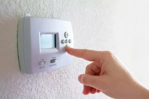 A person adjusts a white wall-mounted thermostat by pressing a button.