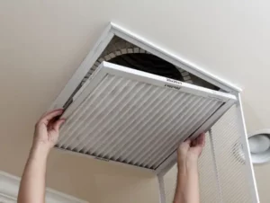 Person installing or removing an air filter from a ceiling vent.