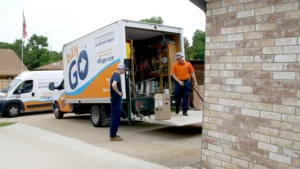 Workers unload equipment from a billyGO truck parked in a driveway beside a brick building, showcasing the efficiency and reliability of their membership plan.