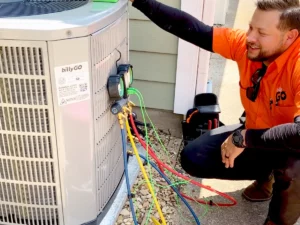 Technician in an orange shirt inspecting an air conditioning unit with various colored cables attached.